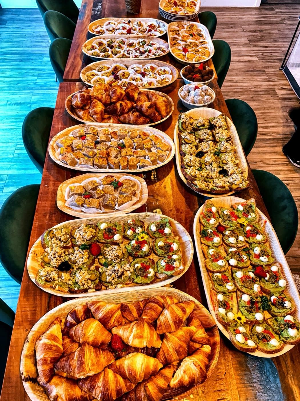 Lange Frühstückstafel im Büro mit Croissants, Avocado-Broten, Eiermuffins und Bananenbrot